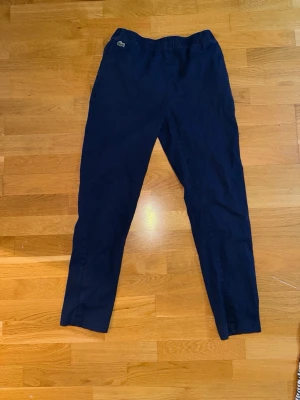 Lacoste Byxor marinblå - Mörkblå chino/mjukis-byxor med resår i midjan och raka ben. Byxorna har en liten broderad logga framtill och fickor på sidorna samt en bakficka. Perfekta för en avslappnad stil och sköna att ha på sig hela dagen. Storleken ser ni på sista bilden. Byxorna är i ett använt skick men har fortfarande mycket att ge, köptes för ca 800, kom gärna med prisförlag!