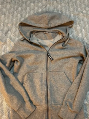 Grå zip hoodie från Björn Borg - Snygg grå hoodie från Björn Borg med dragkedja framtill och två fickor. Tillverkad i mjukt sweatshirtmaterial och har en klassisk huva med dragsko. Perfekt för chill dagar eller när du vill ha en enkel och stilren look.