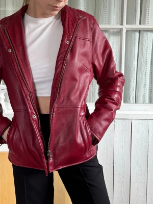 Röd skinnjacka med dragkedja - Snygg röd skinnjacka med dragkedja framtill och två fickor på sidorna. Jackan har en rak passform och coola detaljer med tryckknappar vid kragen. Perfekt för dig som vill sticka ut med en färgstark look.