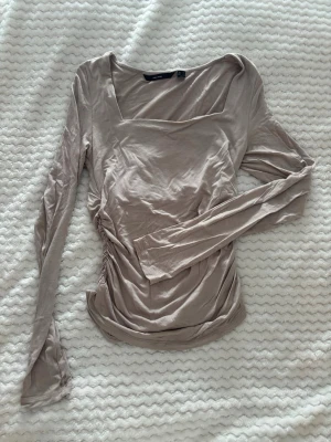 Beige långärmad topp Vero Moda - Säljer en beige långärmad topp från Vero Moda med fyrkantig ringning och rynkade sidor. Tunn och mjuk i materialet, perfekt till alla dina outfits. Passar dig som gillar stilrena och enkla plagg med en twist.