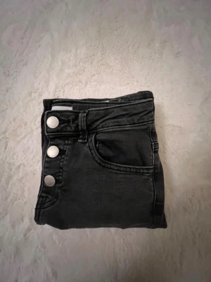 Svarta jeans med silverknappar🖤 - Snygga svarta jeans med tre stora silverfärgade knappar i midjan och klassiska fickor fram. Jeansen har en rak passform och är tillverkade i ett stretchigt denimtyg som sitter bekvämt. Perfekta för dig som gillar en stilren och enkel look.