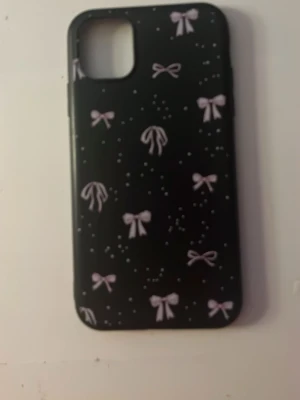 Svart mobilskal med rosett-mönster (Iphone11) - Snyggt svart mobilskal dekorerat med rosa rosetter och små prickar. Tillverkat i ett tåligt material som skyddar din telefon mot repor och stötar. Priset kan diskuteras.
