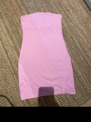 Rosa axelbandslös klänning H&M - Säljer en rosa axelbandslös klänning från H&M Basic. Klänningen är kort och har en enkel, tight passform i mjukt ribbat material. Perfekt för dig som gillar minimalistisk och stilren design.