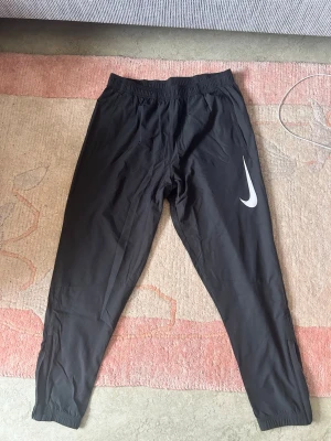 Nike byxor  - Svarta träningsbyxor från Nike med Dri-FIT-teknologi. Byxorna har en elastisk midja och muddar vid bensluten. En vit Nike-logotyp är placerad på vänster ben. Längs sidorna finns reflekterande detaljer. Ny pris på såna är 799kr, pris kan diskuteras!!