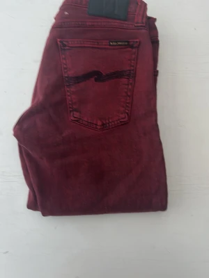 Vinröda jeans från Nudie Jeans - Snygga vinröda jeans från Nudie Jeans med klassisk femficksmodell och vågdetalj på bakfickan. Jeansen har raka ben och är tillverkade i ett mjukt bomullstyg med lite stretch för extra komfort. Perfekta för dig som vill sticka ut med färg.