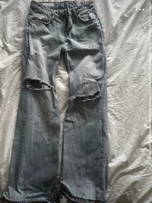 Ljusblå ripped jeans från Zara - Säljer ett par ljusblå jeans från Zara med stora slitningar över knäna och raka ben. Jeansen har klassisk femficksmodell och är tillverkade i denim. Perfekta för en avslappnad och trendig look. Benen är uppsydda ungefär 3-4 cm och passar mig som är 165cm perfekt, ett av benen är därimot hyfsat upptrampat som man tydligt ser på bilderna.