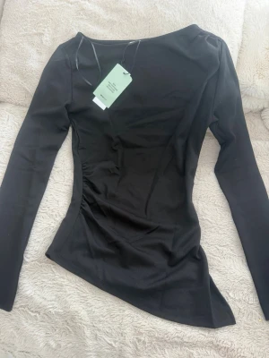 Svart långärmad topp med asymmetrisk kant accepterar bud 💕 - Snygg svart långärmad topp med figurnära passform och asymmetrisk nederkant. Tillverkad i mjukt material som känns skönt mot huden. Perfekt att styla med jeans eller kjol för en trendig look.