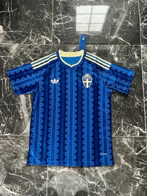 Blå Sverige fotbollströja Adidas - Säljer en blå fotbollströja från Adidas med Sveriges landslagsemblem på bröstet. Tröjan har ett unikt mönster i olika blå nyanser, gula detaljer vid krage och axlar samt klassiska Adidas-ränder. Perfekt för match eller träning!