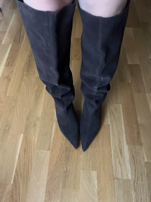 Svarta höga mockastövlar med spetsig tå - Säljer ett par svarta höga stövlar i mocka med slouchy passform och spetsig tå. Stövlarna går upp till knäna. köpta för 1599 kr, helt oanvända och är slut i lager på hemsidan.