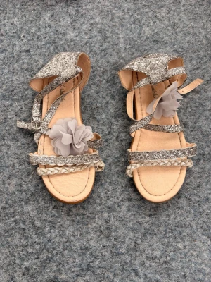 Glittriga sandaler med blomdetalj strl 33 - Säljer ett par silvriga sandaler från LC Waikiki med glitter och justerbar rem med spänne runt ankeln. Strl 33 och användna så jag accepterar vilka bud som helst. 
