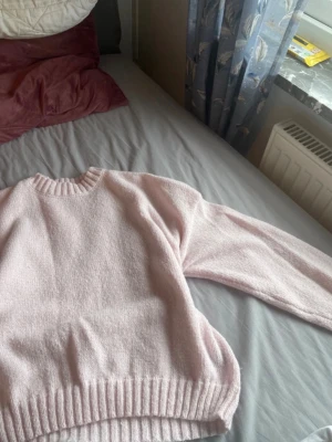 Ljusrosa stickad tröja - Mysig ljusrosa stickad tröja med rund halsringning och ribbade muddar vid ärmslut och nederkant. Tröjan har en avslappnad passform och är perfekt för kyliga dagar. Materialet känns mjukt och behagligt mot huden.