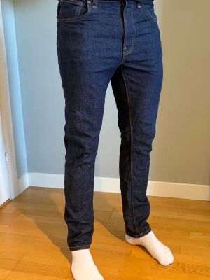 Nudie jeans slim fit - Snygga mörkblå jeans i slim fit-modell med klassiska fem fickor och kontrastsömmar. Jeansen har normal midja och raka ben. Tillverkade i ett stadigt denimtyg som ger en tidlös look. Är 185 cm. Använda ett fåtal gånger