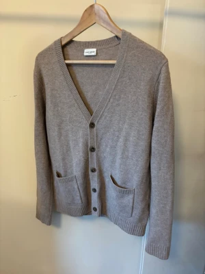 Beige cardigan - Klassisk beige stickad kofta med v-ringning och knappar framtill. Två fickor framtill och ribbade muddar vid ärmslut och nederkant. Perfekt att slänga över en t-shirt eller skjorta för en chill look.