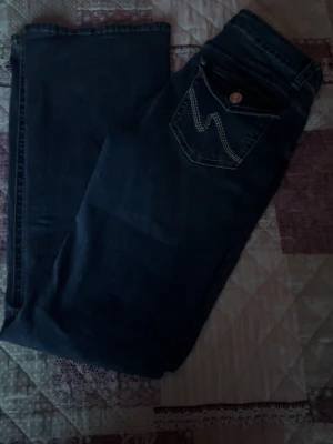 Mörkblå jeans med broderad bakficka - Snygga mörkblå jeans med bootcut-modell och dekorativ ficka bak med vit söm i zigzag-mönster. Klassisk femficksdesign och knappstängning. Perfekta till en avslappnad stil och passar till det mesta. Tillverkade i denim med skön stretch.helt oanvända utan prislapp 