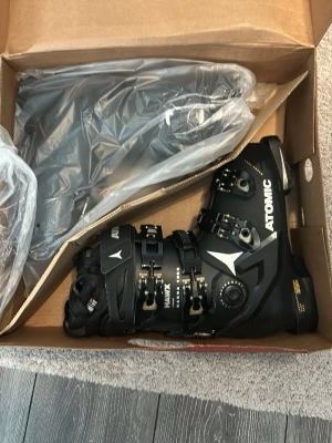 Atomic Hawx Magna 105 pjäxor svart/guld - Säljer ett par Atomic Hawx Magna 105 S W GW pjäxor i svart med detaljer i guld. Skalet har bred passform (102 mm) och flera spännen för optimal justering. Perfekta för dig som vill ha stabilitet och komfort i backen.