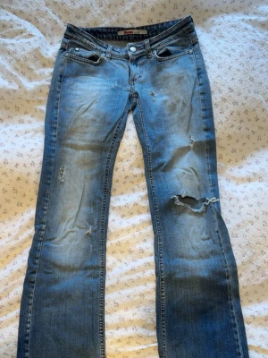 Blå vintage jeans från only Jeans - Ett par blåa vintage jeans från One Jeans med slitningar och hål på benen för en cool, avslappnad look. Jeansen har klassisk femficksdesign, knappgylf och raka ben. Perfekta för dig som gillar en trendig och edgy stil.