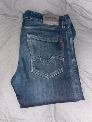 Blå Replay jeans med vintage look - Säljer ett par blå Replay jeans i modellen Waitom med snygg vintage tvätt och klassiska detaljer. Jeansen har raka ben, fem fickor och coola röda sömmar vid fickan. Perfekta för dig som gillar en avslappnad men stilren look.