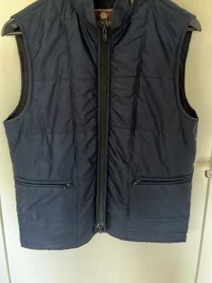Mörkblå dunväst från Morris - Snygg och sällsynt mörkblå dunväst från Morris Heritage med dragkedja framtill och två praktiska fickor med dragkedja. Västen har en klassisk, rak passform och quiltad design. Säljer den för att den är för liten, skulle säga att den passar någon upp emot 180 cm. Pris ej hugget i sten🪨🙌