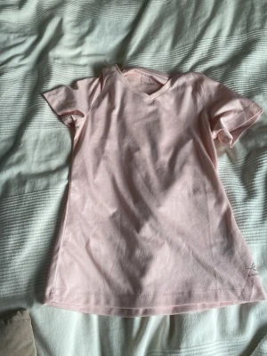 Ljusrosa v-ringad t-shirt - Söt ljusrosa t-shirt med v-ringning och korta ärmar. Enkel och stilren design som passar perfekt till jeans eller kjol. Tillverkad i mjuk bomull för en bekväm känsla hela dagen.