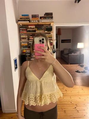 Gul volangig linnetopp med spets - Supersöt ljusgul linnetopp med volangig nederdel och broderade spetsdetaljer. Djup v-ringning och smala axelband ger en luftig och somrig känsla. Perfekt för varma dagar och enkel att styla med jeans eller kjol. Passar för S och XS