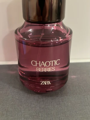 ZARA Chaotic Berries parfym - En snygg parfymflaska från ZARA i lila glas med svart lock. Doften heter Chaotic Berries och flaskan har en modern, rund form. Perfekt för dig som gillar bäriga och fruktiga dofter.