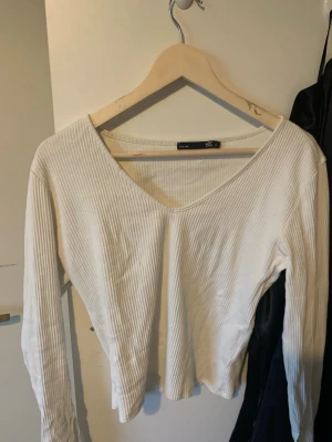 Vit ribbad långärmad topp 157 - Vit långärmad topp från 157 med v-ringning och ribbad struktur. Toppen har en figurnära passform och är perfekt att styla med jeans eller kjol. Enkel och stilren design som passar till många olika looks. Passar M