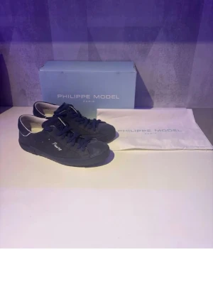 Philippe Model blå mockasneakers ÄKTA - Snygga blå sneakers från Philippe Model i mocka med mörkblå snörning och vit detalj vid hälen. Klassisk låg modell med diskret logga på sidan och bekväm innersula. Perfekta för dig som gillar stilrena och trendiga skor.