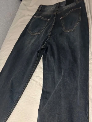 Mörkblå raka jeans med kontrastsömmar - Säljer ett par mörkblå jeans med raka ben och klassiska kontrastsömmar. Jeansen har två bakfickor med detaljerade sömmar och bälteshällor. Materialet är denim och de har en tidlös look som passar till det mesta.