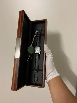 Svensk märke - d’Heritage (Helt Ny) först tillkvarn  - Stilfullt armbandsur från Cosmos d'Héritage med en rektangulär boett och en klassisk urtavla med romerska siffror. Klockan har en svart läderarmband som ger en sofistikerad touch. Baksidan av boetten är graverad med "1986 d'Héritage".   Elegant & tidlös design som passar både vardag och fest. Ny & oanvänd, levereras i skyddad förpackning Ord. pris: 1599 kr  Nu pris: 599 kr Helt ny