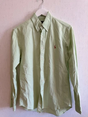 Ljusgrön skjorta från Polo Ralph Lauren - Snygg ljusgrön skjorta från Polo Ralph Lauren i slim fit-modell. Skjortan har klassisk krage, långa ärmar och knappar framtill. Tillverkad i stretchig bomull och har den ikoniska broderade loggan på bröstet.