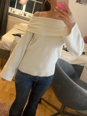 Vit off shoulder stickad tröja - Säljer en vit stickad tröja med off shoulder-design och bred krage. Tröjan har långa ärmar och ribbstickade muddar vid ärmslut och nederkant. Perfekt för dig som gillar en stilren och trendig look.