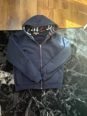 Marinblå burberry zip up - En riktigt snygg Marinblå burberry! Den är i jätte fin skick, den är i storlek L men passar även M! Inga solbrännor eller grova defekter kolla sista bilden där vi har ett litet håll som inte syns om man inte öppnar och börjar kolla riktigt noggrant + snörren är borttappade annars är detta en jätte fin tröja som sticker ut för det är inte så många som har denna färgen. Säljer denna för 620 priset kan eventuellt sänkas vid snabb affär och köp direkt🔥. Kom inte med dumma priser🤝