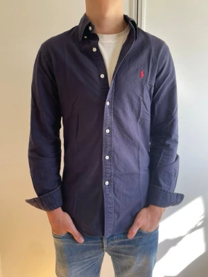 Mörkblå ralph Lauren skjorta - Klassisk mörkblå skjorta från Ralph Lauren med röd broderad logga på bröstet. Skjortan är i mycket fint skick och är perfekt inför sommaren🤩☀️ nypris:1599kr mot mitt pris:449kr✅ har du några frågor så är det bara att skriva och priset kan självklart diskuteras vid snabb och smidig affär😃👍