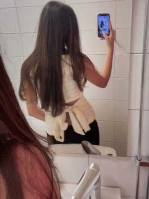 Öppen ryggtröja  - Säljer en snygg vit omlott topp med breda axelband och knyt i ryggen. Toppen är ärmlös och har en ribbad struktur som ger en cool look. Perfekt för dig som gillar stilrena och trendiga plagg.