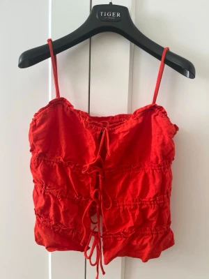 Röd linnetopp med snörning - Trendig röd linnetopp med smala axelband och snygg knytning fram. Hm storlek xs.
