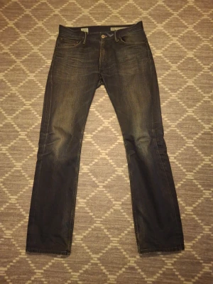Svarta jeans Tommy Hilfiger Ryder - Säljer ett par svarta jeans från Tommy Hilfiger, modell Ryder. Jeansen har raka ben och klassisk femficksdesign. Materialet är crete coated denim som ger en snygg finish. Perfekta för dig som gillar stilrena och tidlösa jeans.