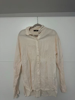 Beige långärmad skjorta från Bik Bok - Säljer en stilren beige / aprikos skjorta från Bik Bok med klassisk krage och knappar framtill. Skjortan är tillverkad i ett linnematerial och har långa ärmar med knappslå. Perfekt för dig som gillar en enkel och avslappnad look.🤗