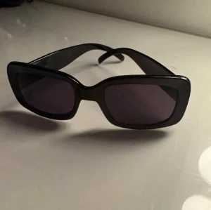 Svarta rektangulära solglasögon - Snygga svarta solglasögon med rektangulära bågar och mörka glas. De har en chunky design som ger en trendig vibe och passar perfekt till alla outfits. Tillverkade i plast för en lätt och bekväm känsla.