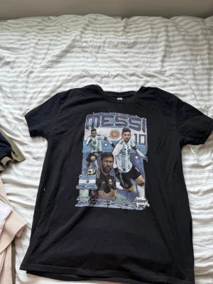 Svart Messi t-shirt med tryck - Cool svart t-shirt med stort Messi-tryck på framsidan. Motivet visar flera bilder av Messi i argentinska landslagströjan och texten 'World Champion'. T-shirten har rund hals och korta ärmar, perfekt för dig som älskar fotboll och vill sticka ut. Storlek L och bra bra skick diskuterar gärna även pris:)