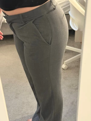 Grå kostymbyxor med raka ben - Snygga grå kostymbyxor med raka ben. Byxorna har två snedställda fickor fram och hällor för skärp. Perfekta för en stilren och trendig look. 
