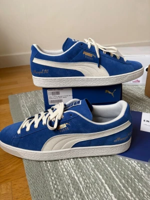 Blå Puma Suede x END sneakers - Blåa Puma Suede sneakers i samarbete med END, med vita detaljer och guldtext. Ovandel i mocka, vita snören och sula. Snygg retrostil med 'END.' och '94' broderat på hälen samt 'Mangal 00' i guld på sidan.