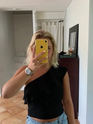 Svart oneshoulder topp med volang - Snygg svart oneshoulder topp med volangdetalj framtill. Toppen är croppad och har en tight passform, perfekt till jeans eller kjol.☀️❤️❤️