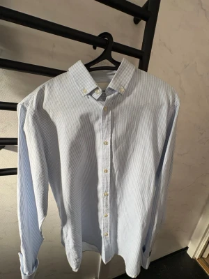 Blårandig skjorta Shine Original -  En aldrig använd snygg blårandig skjorta från Shine Original. Klassisk krage med knappar och lång ärm. Perfekt för dig som gillar stilrena och fräscha skjortor med en tidlös look.