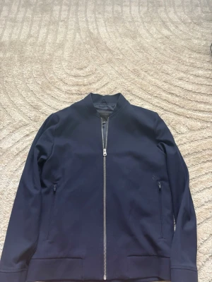 ELVINE jacka  - Snygg mörkblå bomberjacka från elvine med hel dragkedja framtill och två fickor med dragkedja. Jackan har en stilren design och ribbade muddar vid ärmslut och nederkant. Perfekt för dig som gillar en clean look. (OANVÄND)