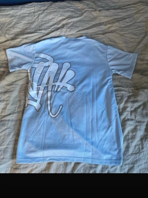 Ljusblå syna world t-shirt - Snygg ljusblå syna world t-shirt med stort vitt grafiskt tryck både fram och bak. T-shirten har rund halsringning och korta ärmar. Perfekt för dig som gillar streetwear och vill sticka ut med en unik design.