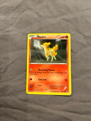 Pokémonkort Ponyta - Samlarobjekt! Pokémonkort med motiv av Ponyta. Kortet har en röd och orange ram, med bild på Ponyta i ett stall. Text och symboler i svart och vitt. Perfekt för dig som gillar Pokémon eller samlar på kort.