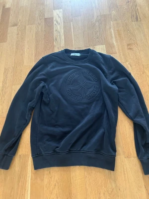 Svart sweatshirt från Stone Island - XL men är som L!                                                 Svart sweatshirt från Stone Island med stort broderat logotypmärke på bröstet. Tröjan har rund halsringning, ribbade muddar och är tillverkad i mjuk bomull. Perfekt för en avslappnad och stilren look.