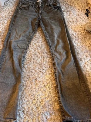 Grå bootcut  jeans från Gina Tricot - Säljer ett par grå jeans från Gina. Tricot  med boot cut passform och klassisk femficksdesign. Jeansen har normal midja och är tillverkade i denim med lätt tvättad look. Perfekta för en avslappnad stil.