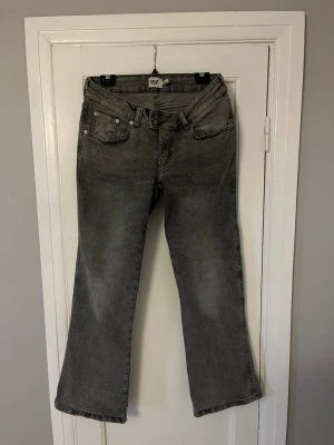 Grå bootcut jeans med broderade fickor - Säljer ett par grå bootcut jeans med snygg tvätt och broderade detaljer på bakfickorna. Jeansen har fem fickor, låg midja och klassisk knappgylf. Perfekta för dig som gillar en avslappnad men ändå trendig stil.