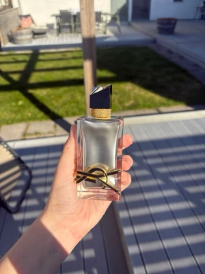 Yves Saint Laurent Libre Eau de Parfum - Säljer en snygg parfymflaska från Yves Saint Laurent, Libre Eau de Parfum. Flaskan är genomskinlig med guldiga detaljer och ett svart lock med guldmönster. Den har en modern, lyxig design och känns riktigt exklusiv att hålla i handen. Ca 95% kvar, använd fåtal gånger.
